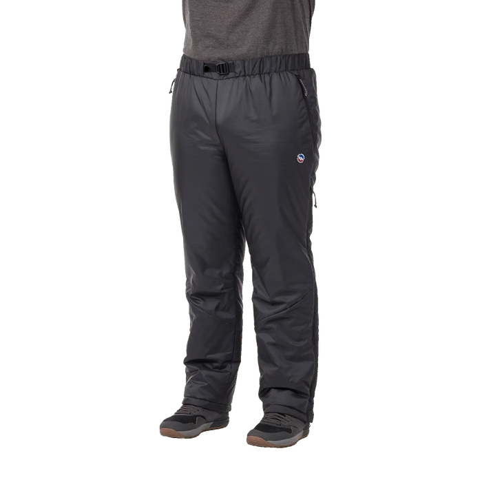 A person wearing Big Agnes Camp Boss Insulated Overpants with FireLine Eco Synthetic insulation and an elastic waistband with a small belt, paired with a gray short-sleeve shirt and gray hiking shoes, stands against a white background.