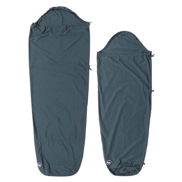 Two dark blue Big Agnes Cotton Sleeping Bag Liners are laid flat. The left is rectangular with a hood; the right is a tapered mummy style. Both feature a small logo at the bottom and are ideal for travel.