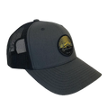 The Big Agnes EST. 2001 Logo Baseball Hat is a dark gray and black trucker hat with a round front patch of a yellow mountain scene, curved bill, adjustable mesh back, and celebrates Big Agnes' 25th Anniversary.