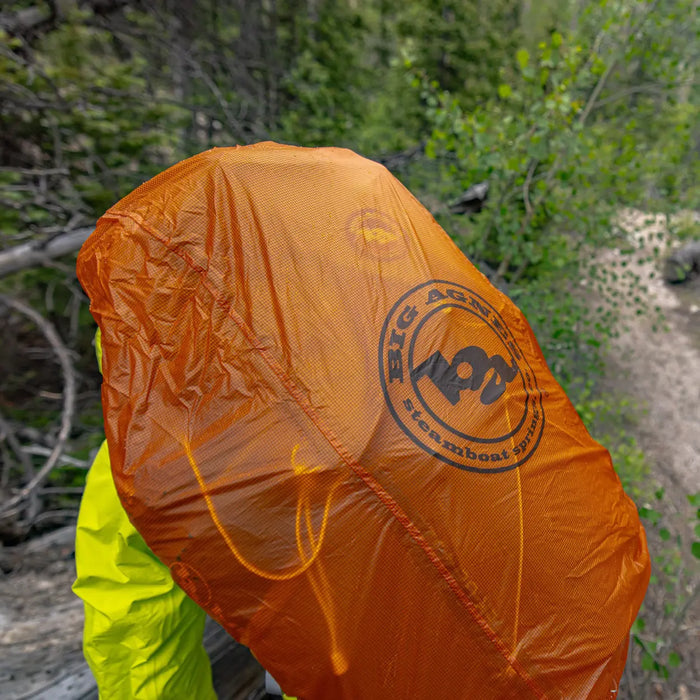 Orange rain cover with a brand logo on a person in a forest setting