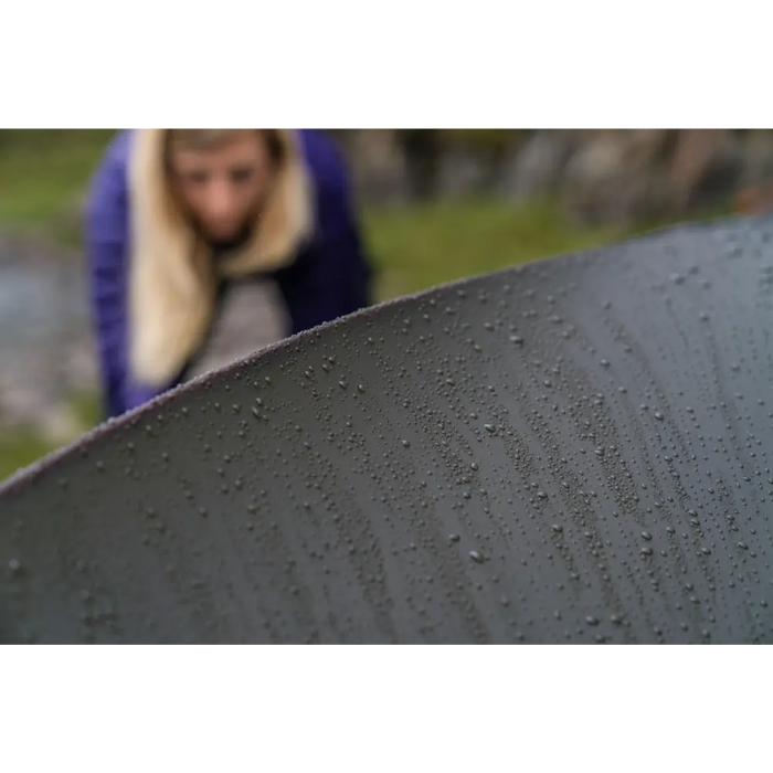 A close-up of a dew-covered tent cleaned with Big Agnes Nikwax Spray On Tent & Gear SolarWash, with a blurred person in a purple jacket and blonde hair outdoors in the background.