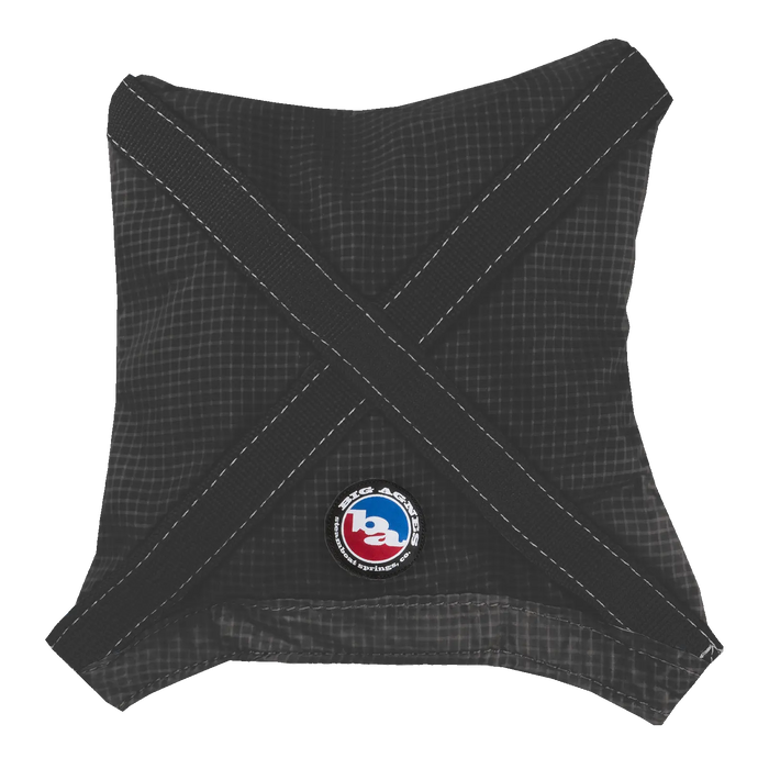 The Big Agnes Superlight Girdle is a black fabric gear bag with a faint grid pattern and two black straps forming an X on the front. A round patch near the bottom center has "ba" in white and blue; perfect as a sleeping bag compression stuff sack.