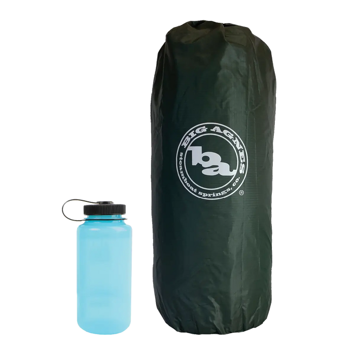 A dark green Big Agnes Tent Stuff Sack 7”x20” stands upright next to a blue water bottle with a black cap, both set against a plain white background.