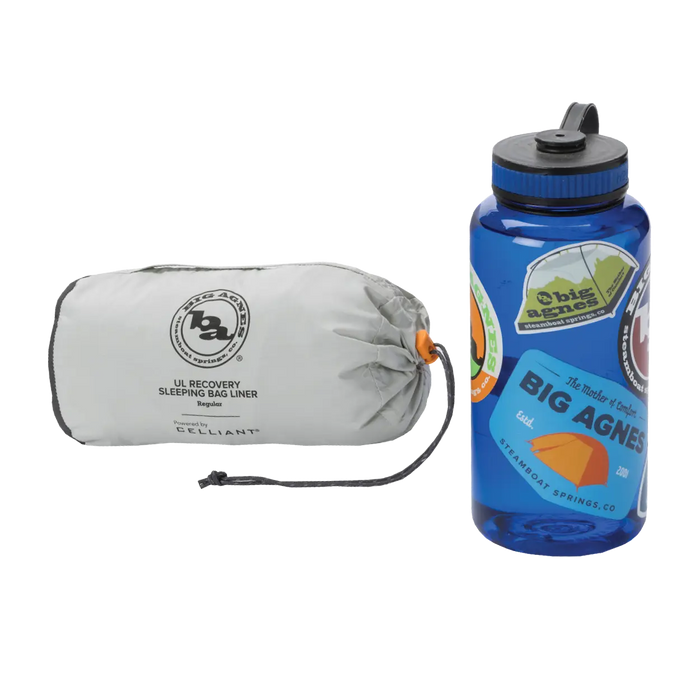 A compact gray Big Agnes UL Recovery Sleeping Bag Liner in a stuff sack sits beside a blue water bottle decorated with colorful stickers.