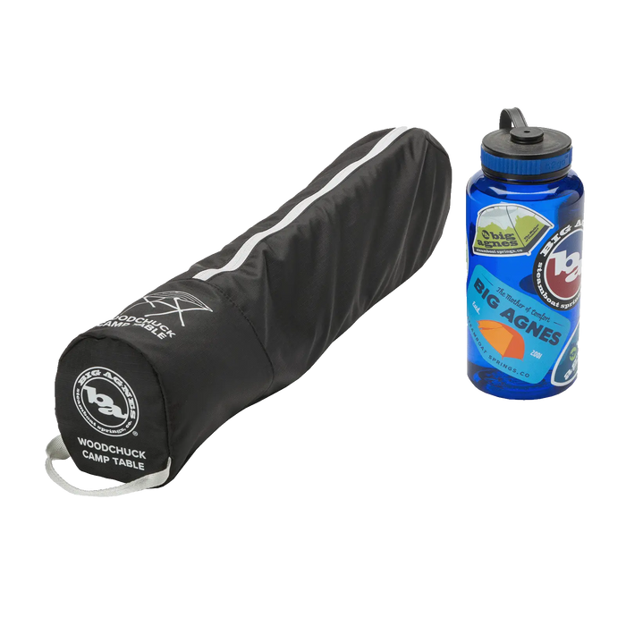 A black, zippered Big Agnes carrying case labeled Woodchuck Camp Table sits next to a blue, sticker-covered reusable water bottle—ideal for transporting your portable camp table on every adventure.