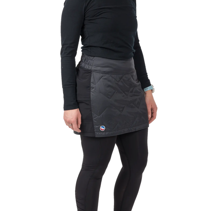 A person wearing a black long-sleeve shirt, black leggings, and the Big Agnes W's Columbine Skirt with diamond quilting stands against a plain white background.